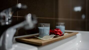 A bathroom with a white sink, two glasses of blue liquid, and a wooden tray with a red rose.