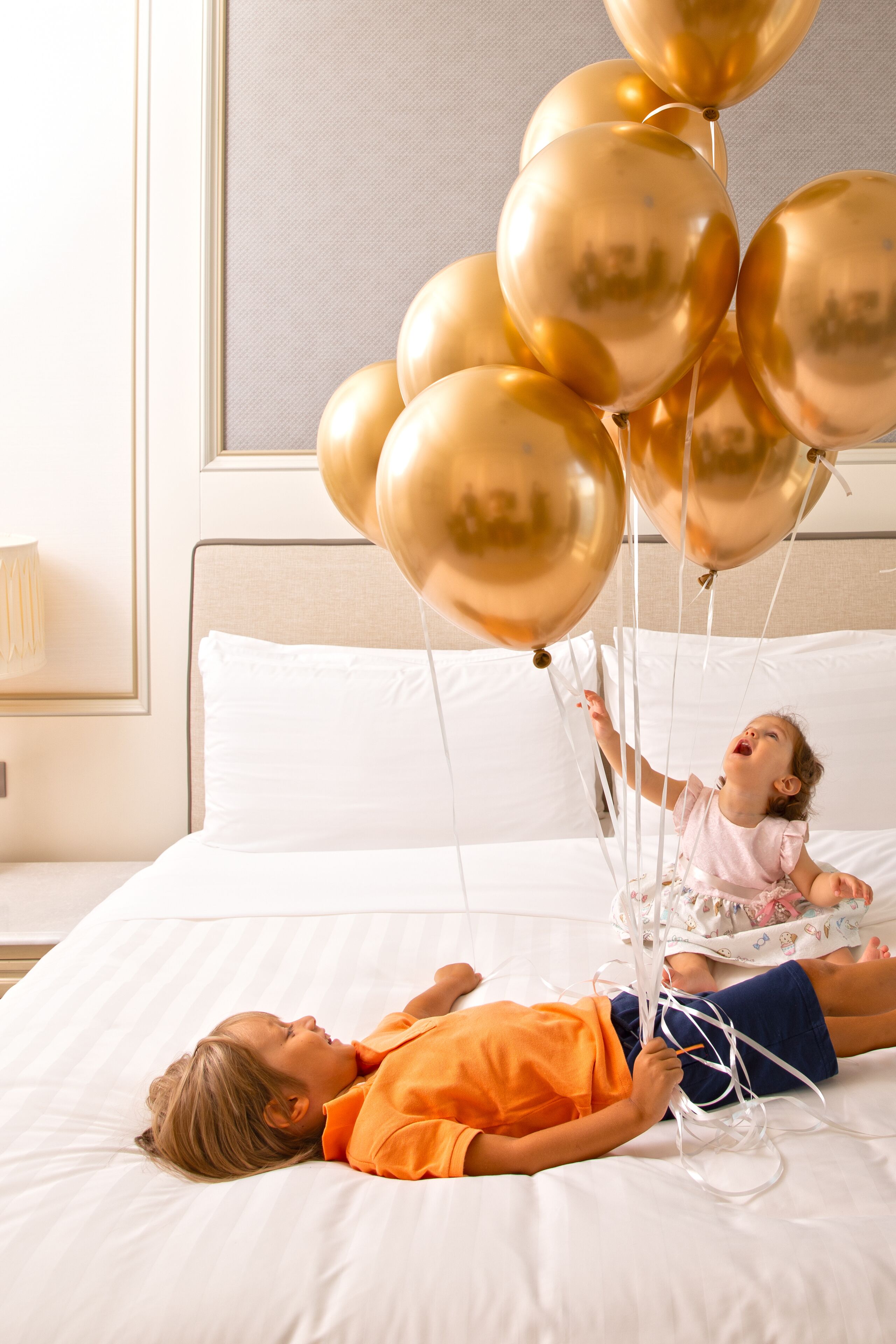 Ett barn och en vuxen ligger på en säng omgiven av gyllene ballonger.