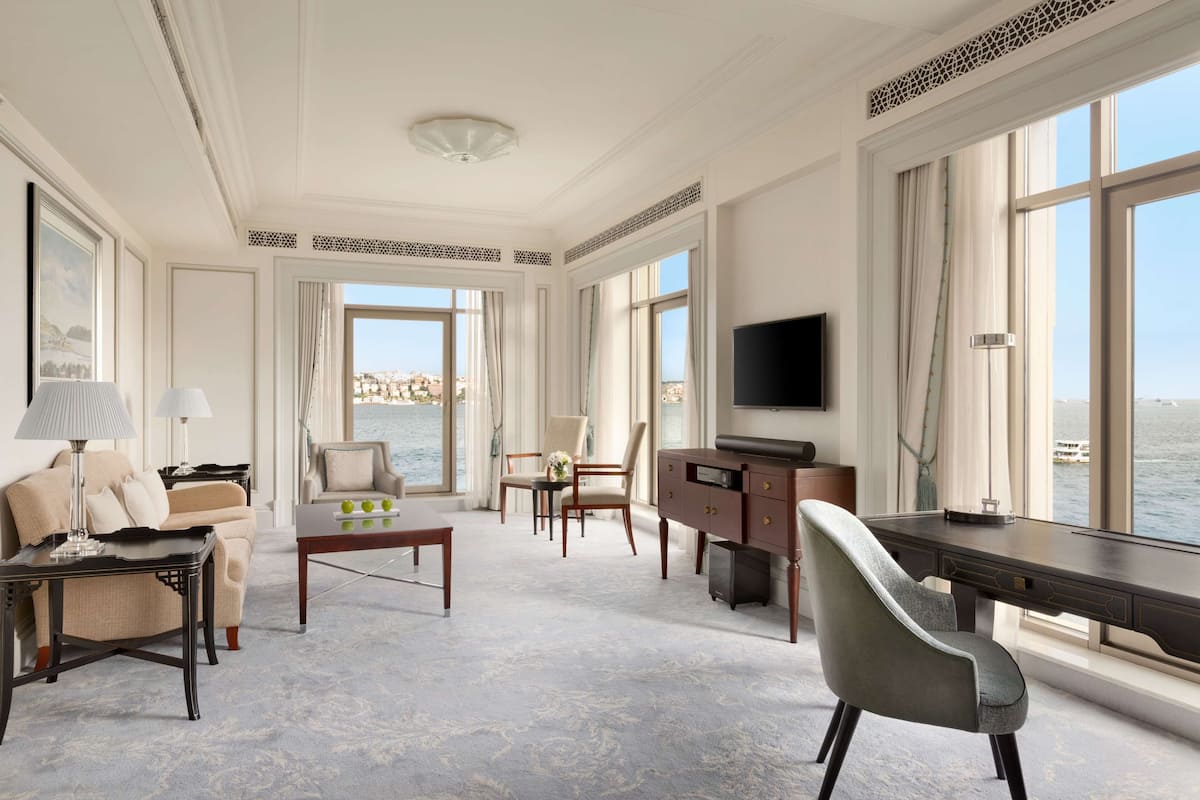 A spacious living room with a large window, a flat-screen TV, and a view of the water.