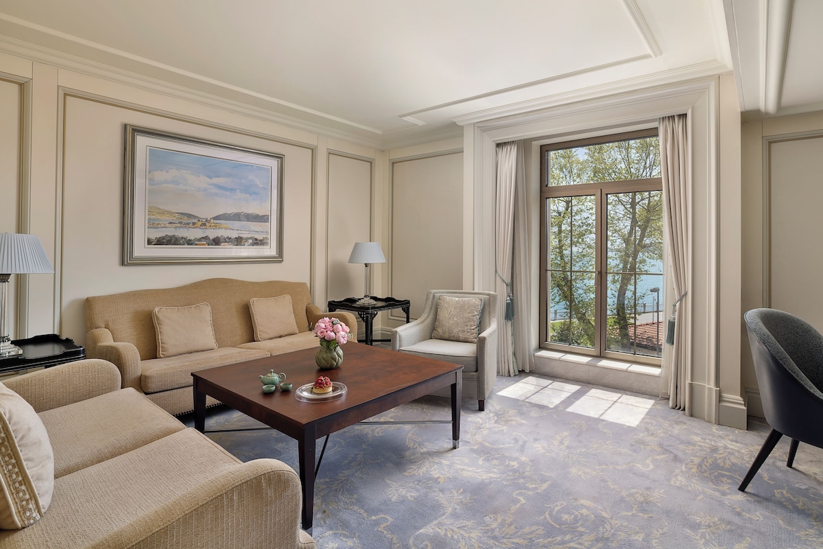 A well-appointed living room with a sofa, armchairs, a coffee table, and a view of the outdoors through large windows.