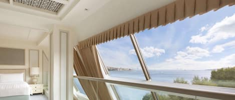A hotel room with a large window offering a sea view, a neatly made bed, and a modern design.