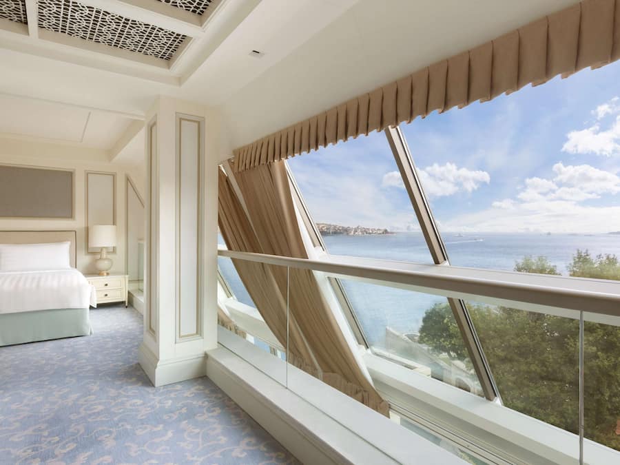 Habitación de hotel con un ventanal grande que ofrece vistas al mar, una cama bien hecha y un diseño moderno.