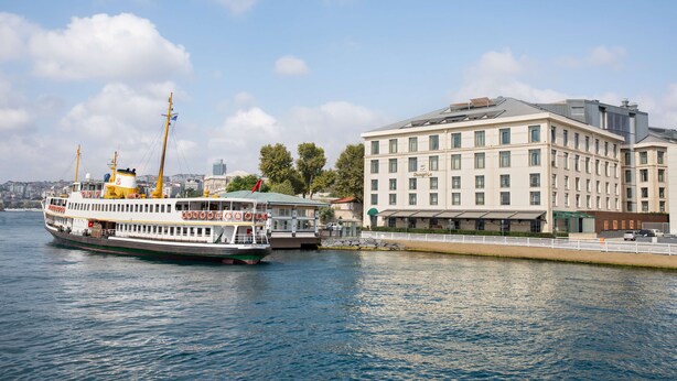 A river cruise ship docked near a hotel with multiple floors and a modern design. - Shangri-La Bosphorus, Istanbul (Istanbul)