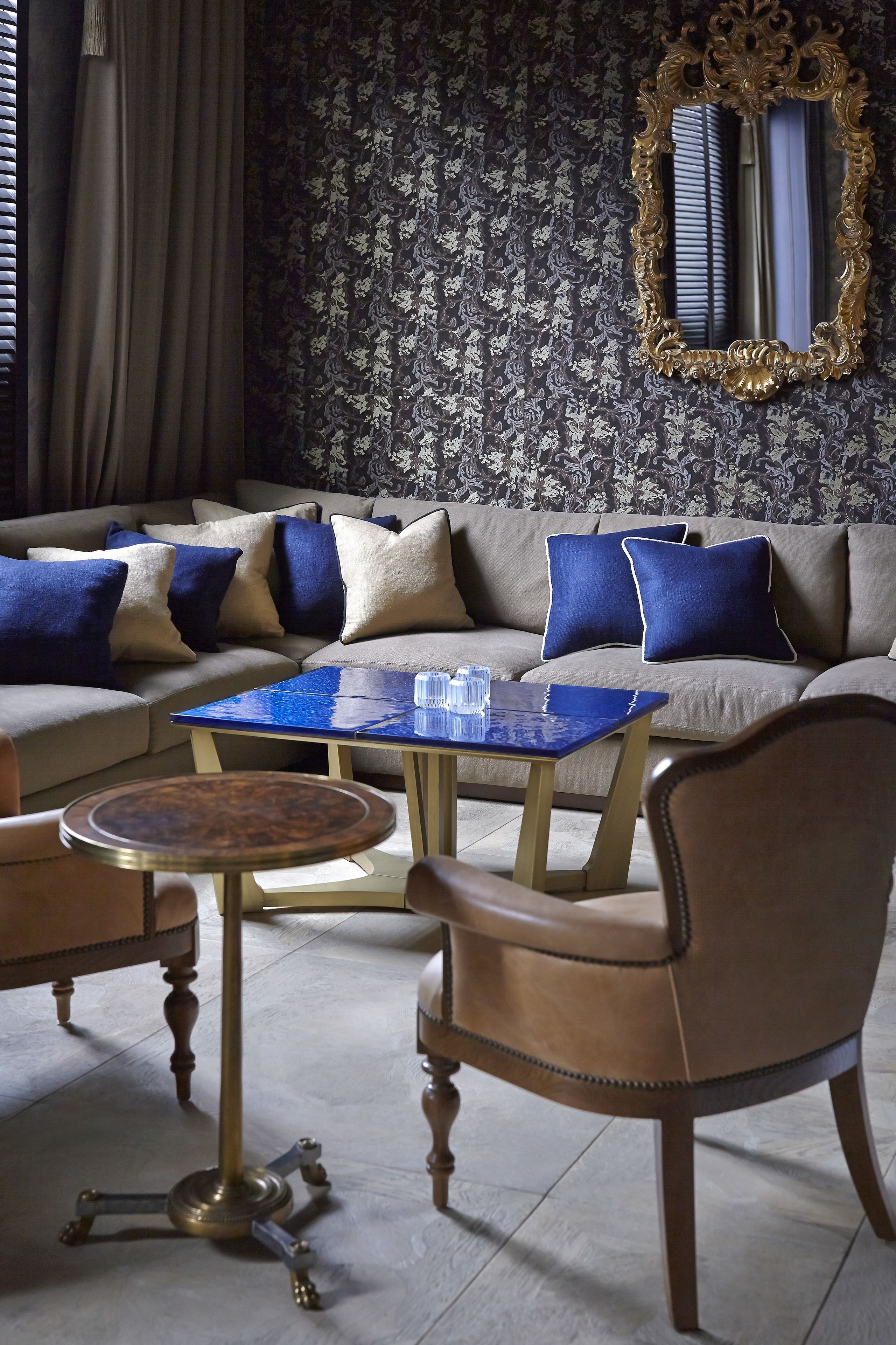 A living room with a sofa, blue cushions, a glass coffee table, and a round table with a brass base.
