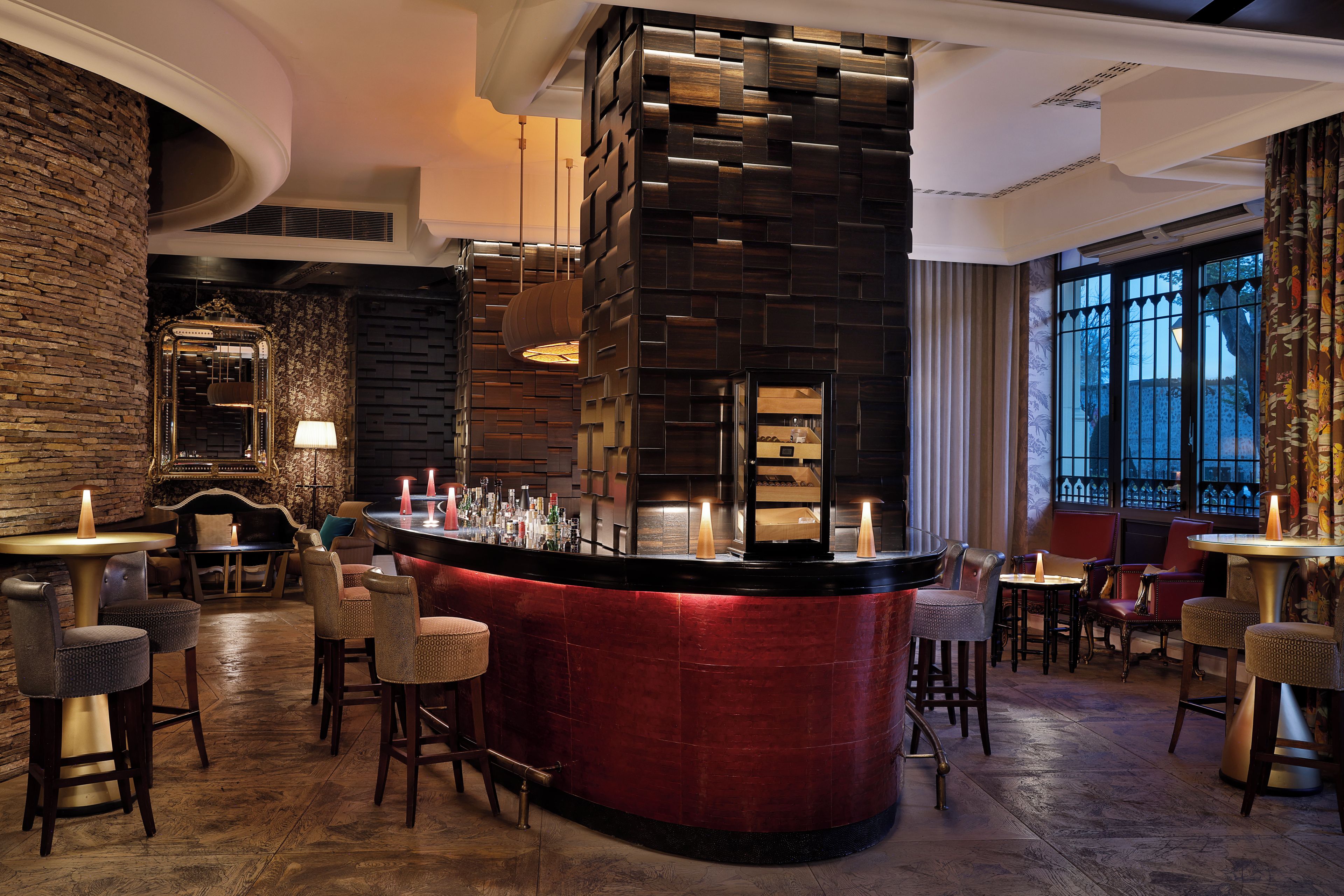 A bar area with a red counter, wooden chairs, and a brick wall.