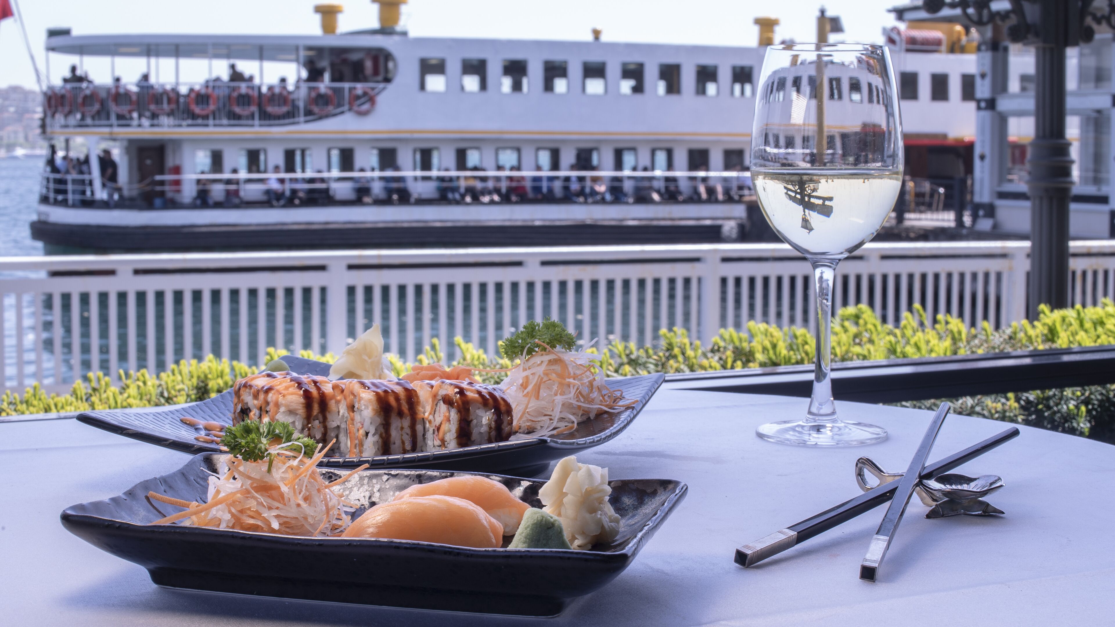 A dining table with a sushi dish, a glass of white wine, and chopsticks.