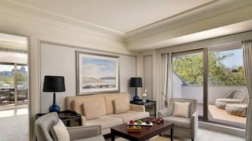 En lys og indbydende stue med en beige sofa, to lænestole, et sofabord med pynteting og et stort vindue med udsigt over grønne områder.