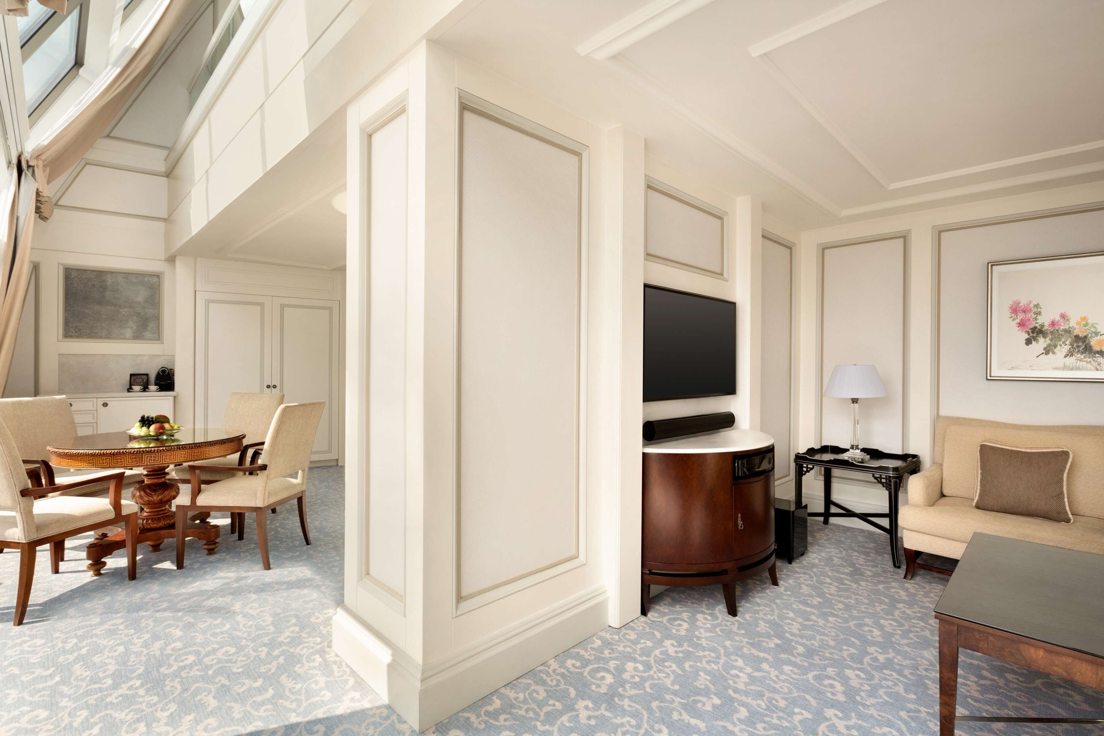 A hotel room with a dining area, a sofa, a TV, and a lamp.