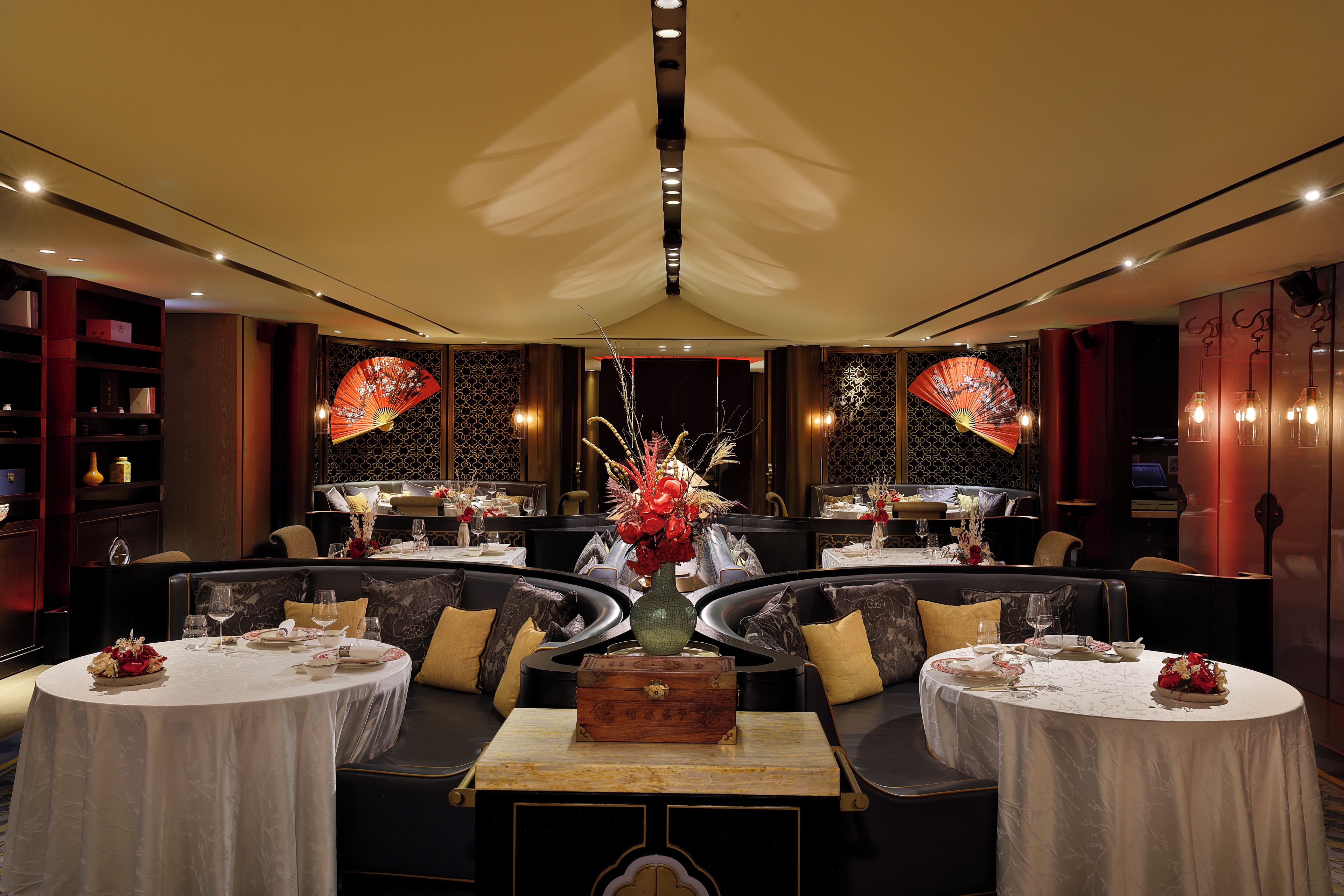 A restaurant with round tables, dark seating, and decorative fans.