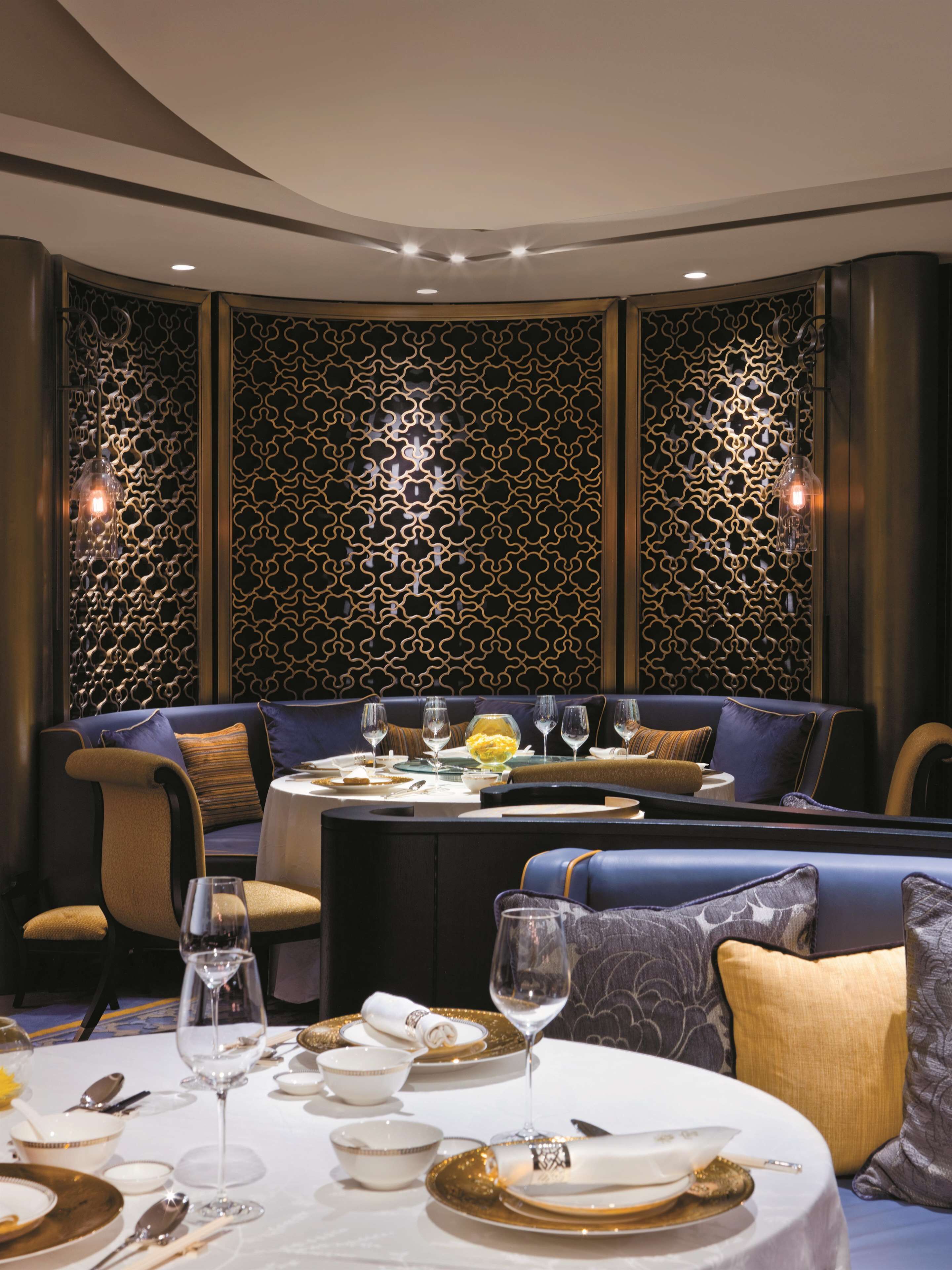 A dining area with a round table set for a meal, a sofa with cushions, and a decorative wall with a geometric pattern.