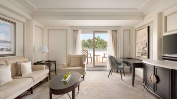 A hotel room with a sofa, a dining table, a TV, and a balcony with outdoor furniture.