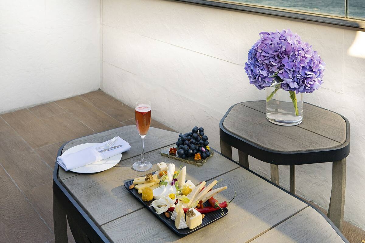 A balcony with a table set for a meal, a glass of drink, and a vase of flowers.