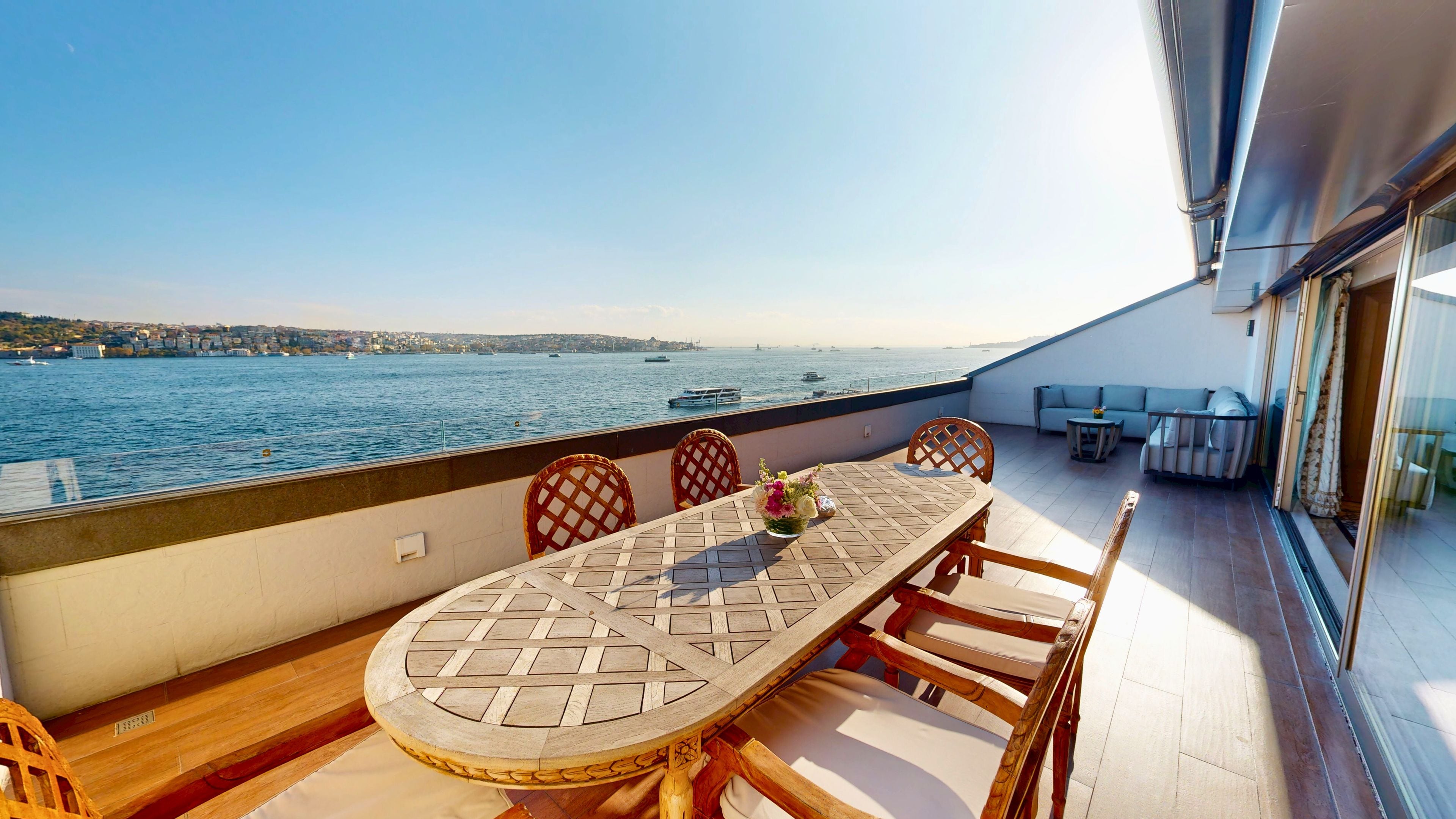 A balcony with a table and chairs, overlooking a body of water with boats.