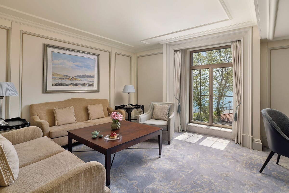 A well-appointed living room with a sofa, armchairs, a coffee table, and a view of the outdoors through large windows.