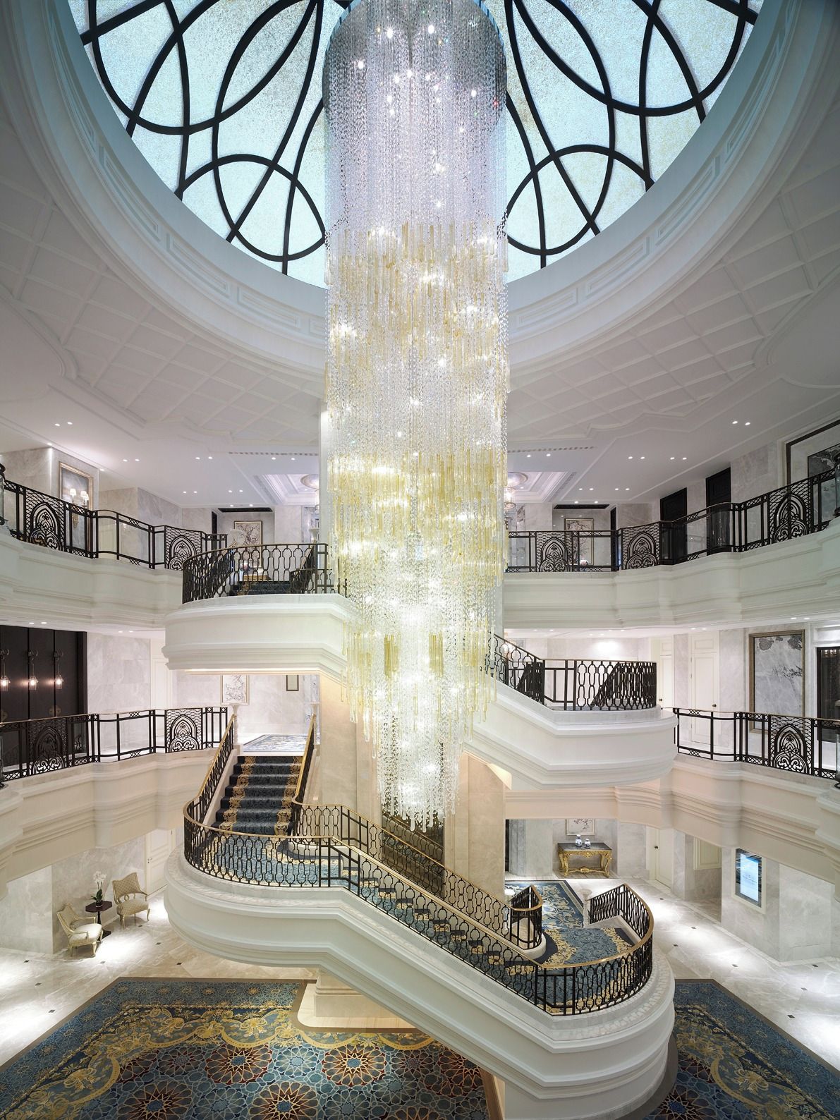 Um amplo átrio com um lustre central, várias varandas e piso ornamental.