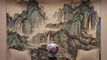 A room with a traditional Chinese landscape painting, two ornate chairs, and a chandelier.