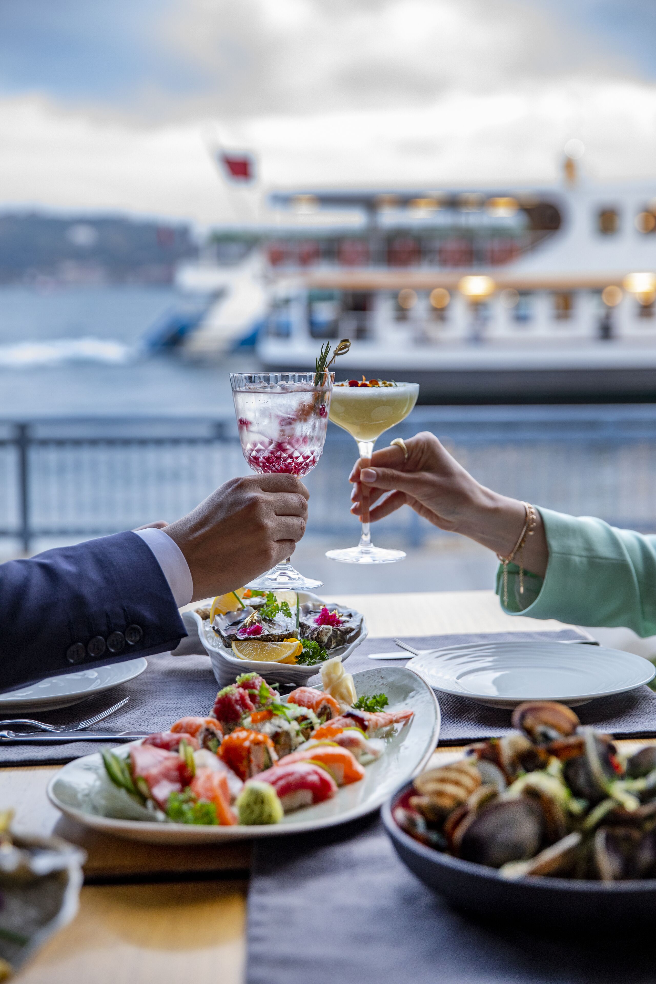 Mesa de jantar com pratos de frutos do mar, um cocktail e vista para um barco na água.