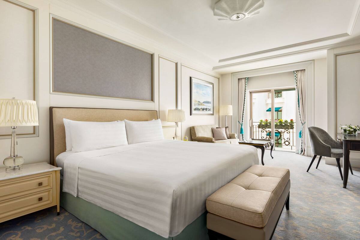 A hotel room with a large bed, a desk, a chair, and a view of the outdoors.