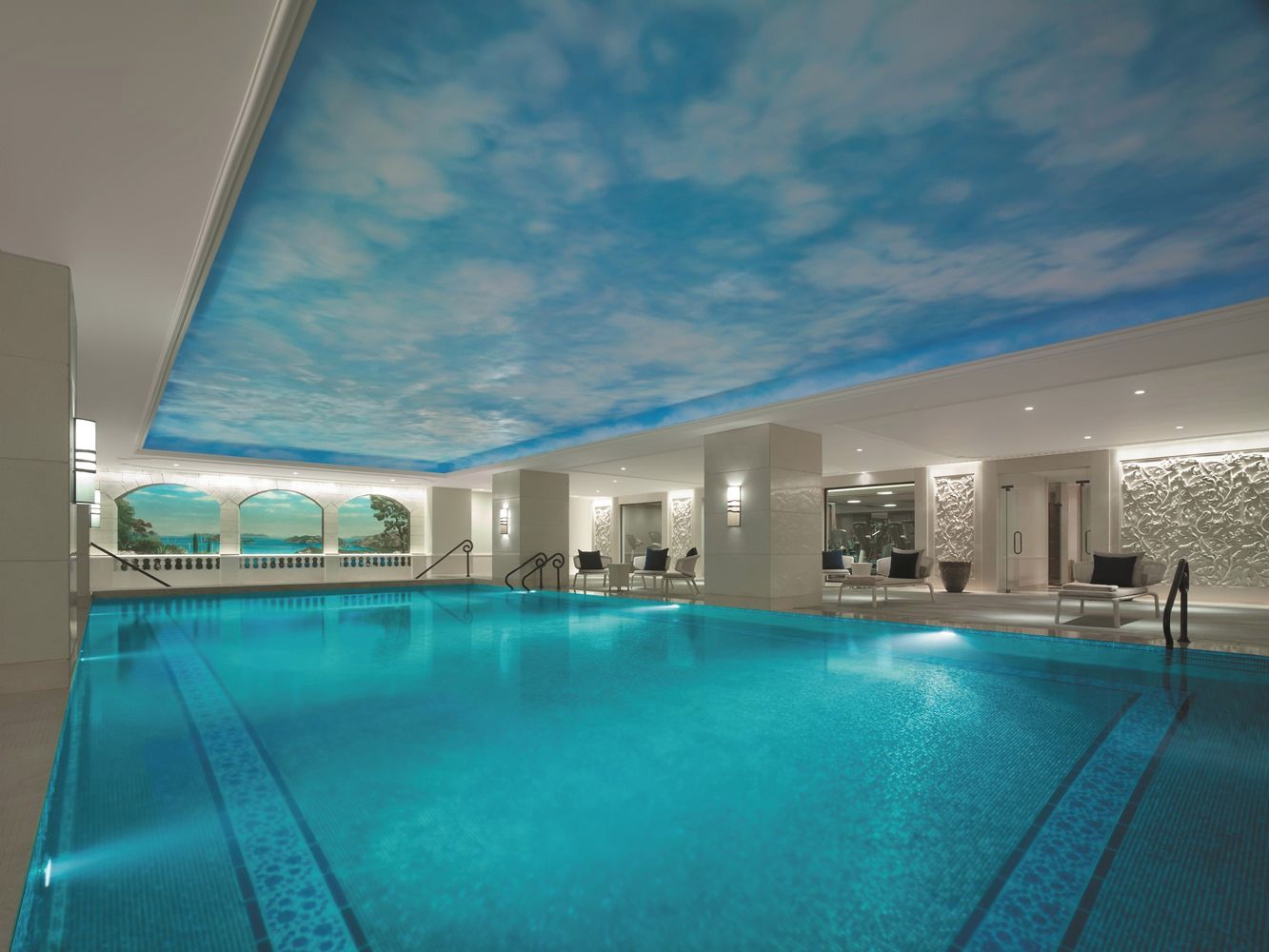 Piscina con affresco al soffitto, sedie a sdraio e zona salotto.