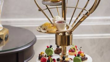 A multi-tiered dessert stand with various pastries and small cakes, set on a marble table against a neutral background.