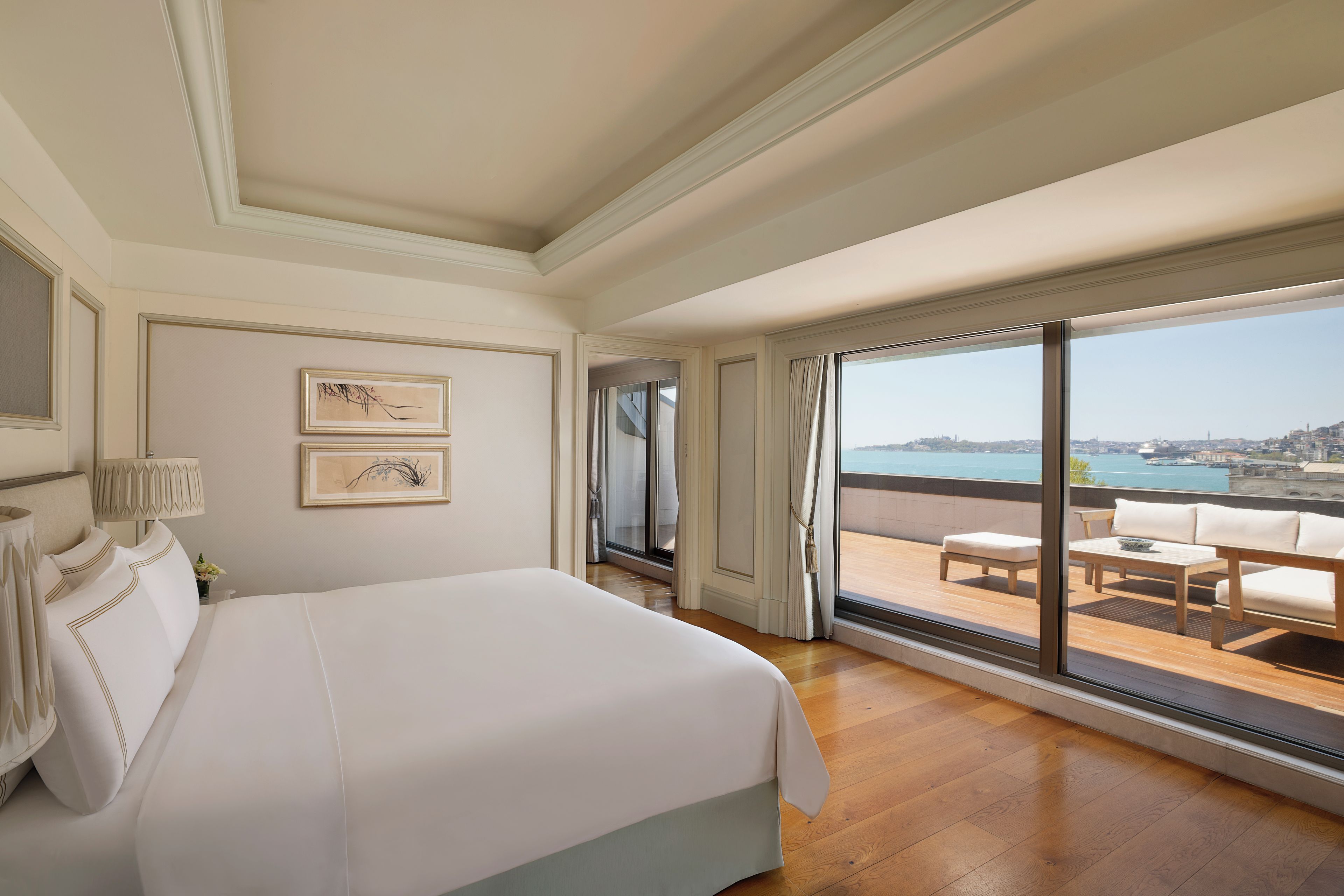 Una habitación de hotel con una cama grande, un balcón con vistas a la ciudad y dos cuadros enmarcados en la pared.
