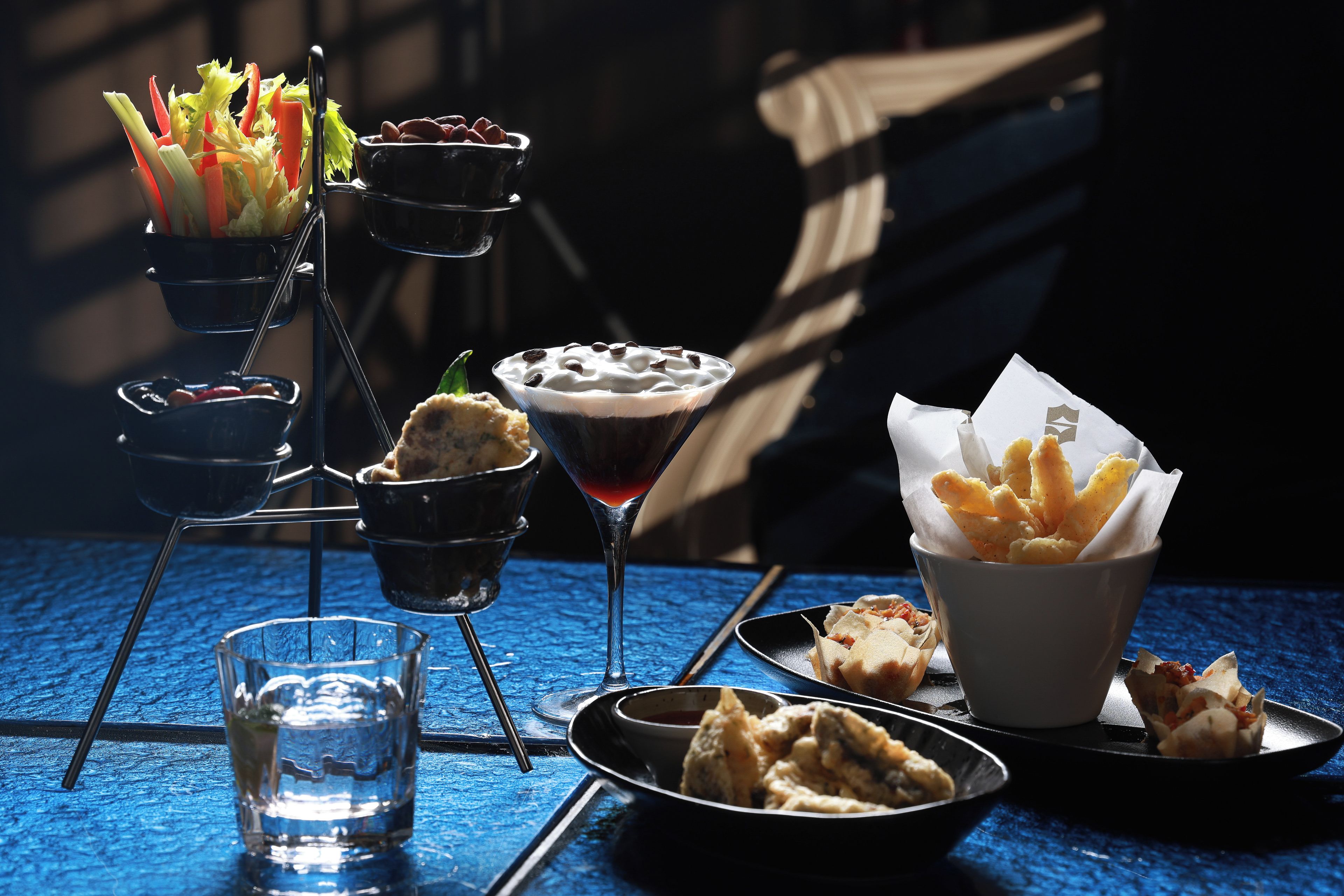 A table set with various food items including a martini glass, a bowl of dessert, and a plate of fried snacks.