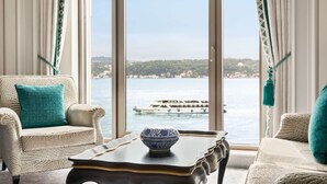 A room with a view of a boat on the water, a chair with a teal pillow, and a table with a blue and white bowl. - Shangri-La Bosphorus, Istanbul (Istanbul)