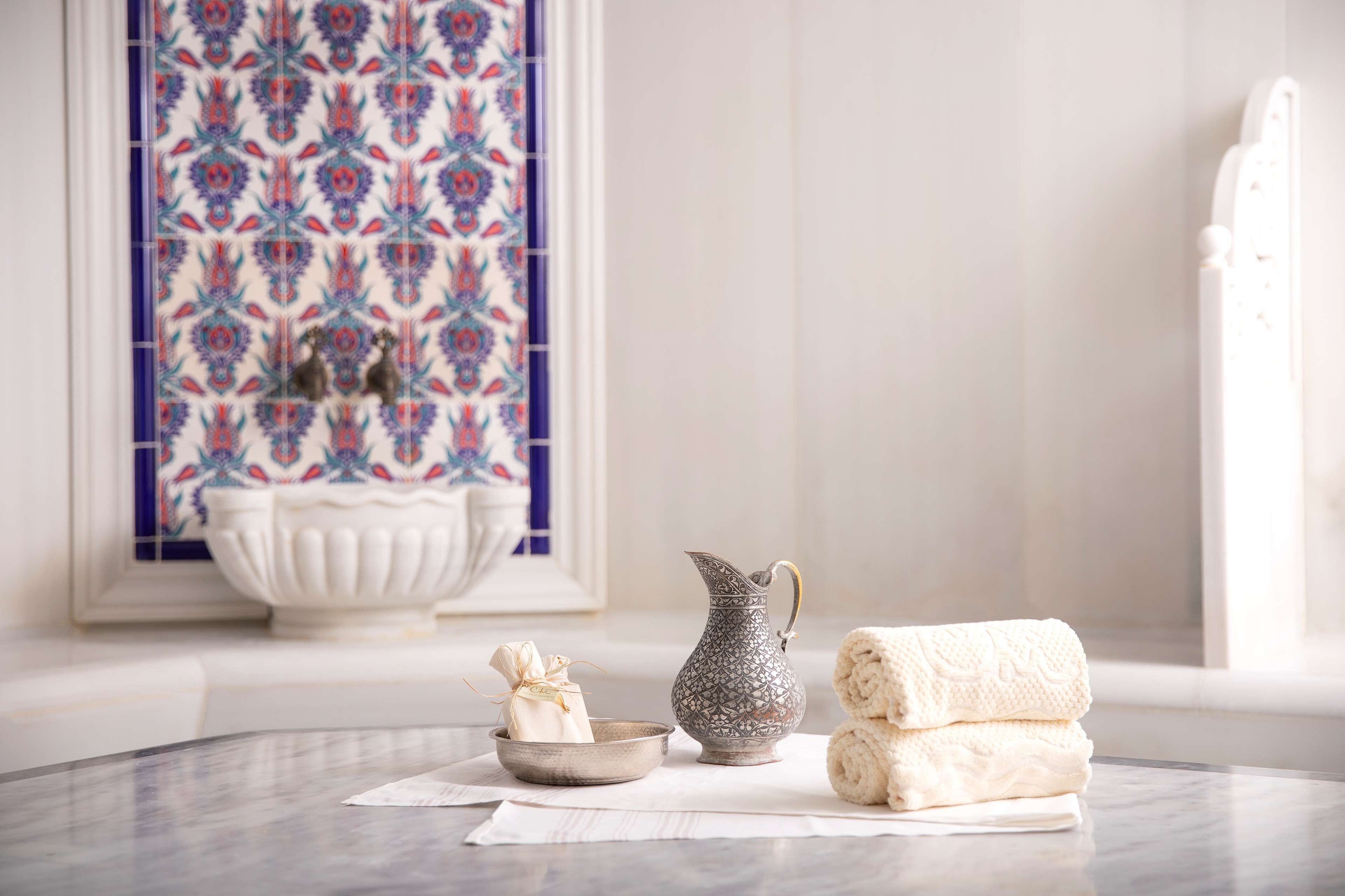 Une salle de bain avec un lavabo en marbre, un pichet décoratif et des serviettes posées sur un plan de toilette en marbre.