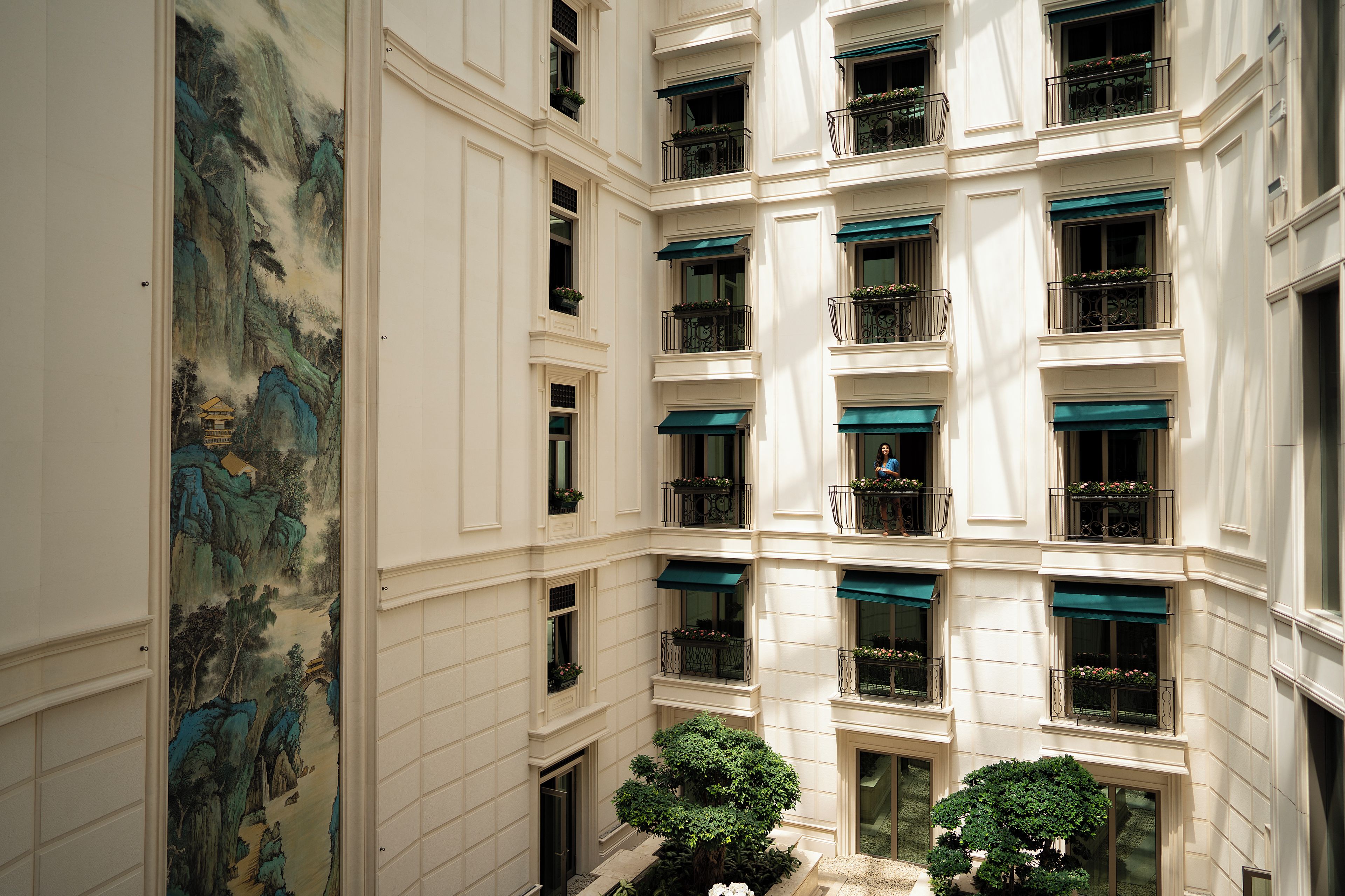 A multi-story building with a classical architectural style, featuring a central courtyard with trees and a mural on the left wall.