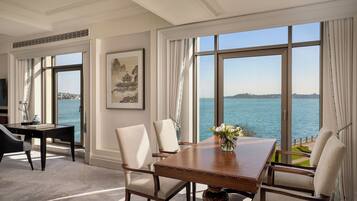 Un comedor con mesa y sillas, ventanas amplias con vista al mar y una obra de arte enmarcada en la pared.