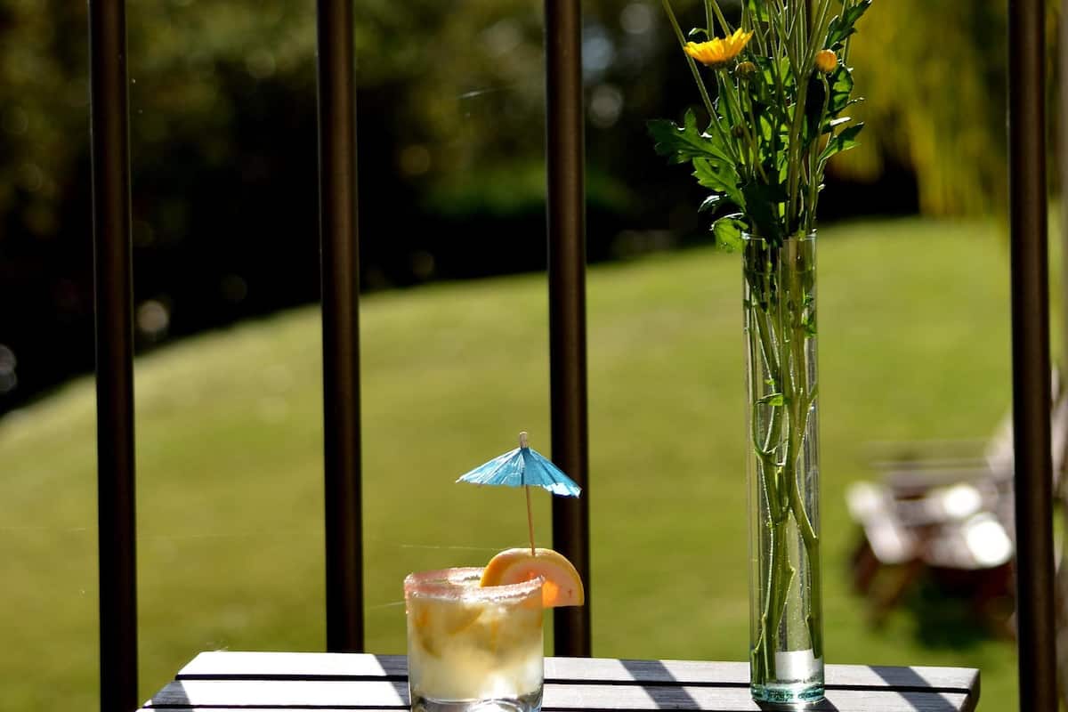 A balcony with a glass table holding a drink and a vase with yellow flowers.