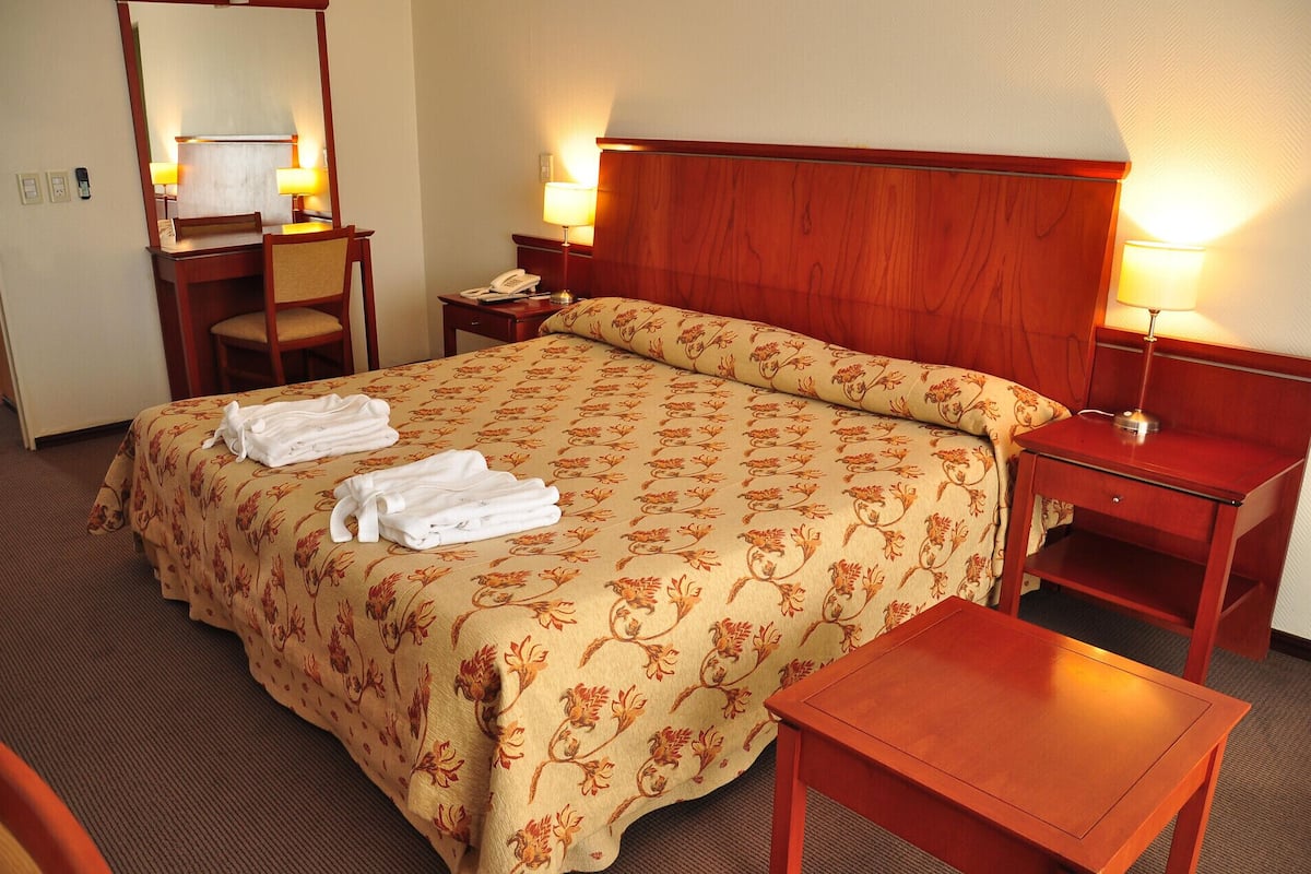 A hotel room with a bed, two bedside tables, a desk with a chair, and a small table.