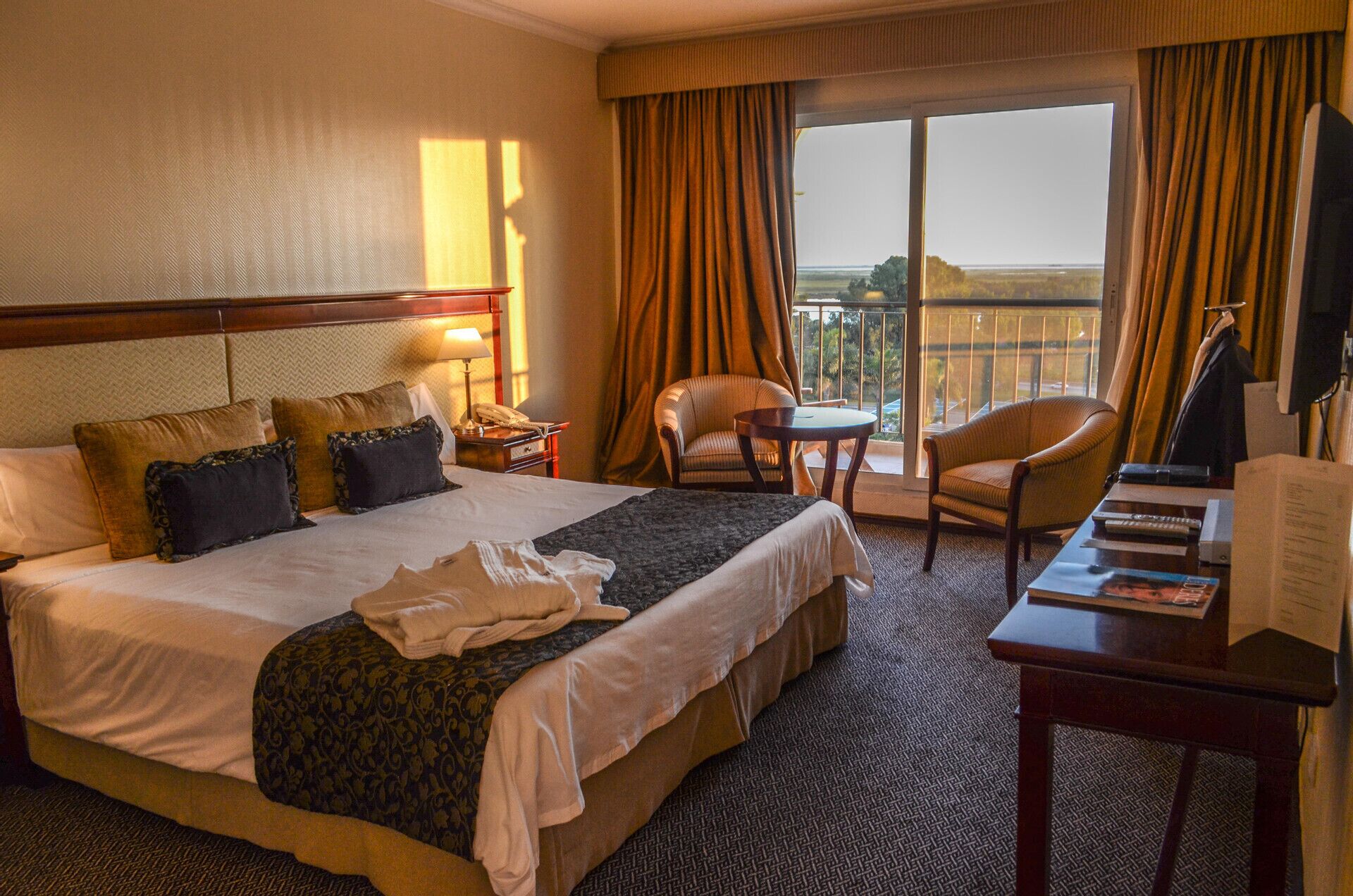 Habitación de hotel con una cama grande, un escritorio, una silla, un teléfono y vistas al exterior.