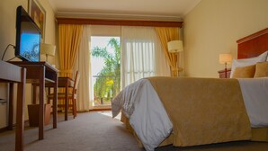 A hotel room with a bed, a desk with a computer, a chair, and a balcony with curtains. - Sol Victoria Hotel, Spa & Casino (Victoria)
