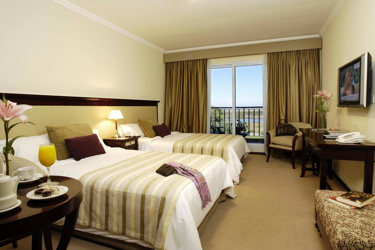 A hotel room with two beds, a desk, a chair, a balcony view, and a TV.