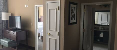 A hotel room with a television on a dresser, a door leading to another room, and a framed picture on the wall.