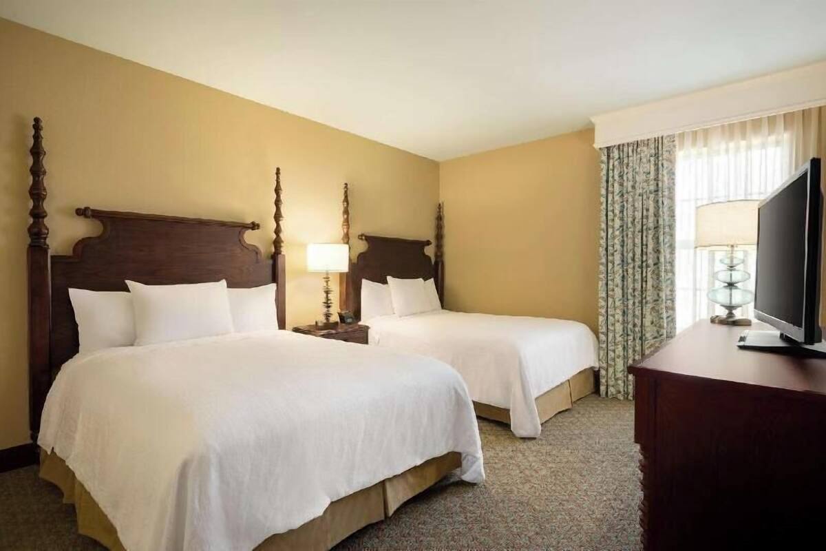 A hotel room with two beds, a television, and a lamp.