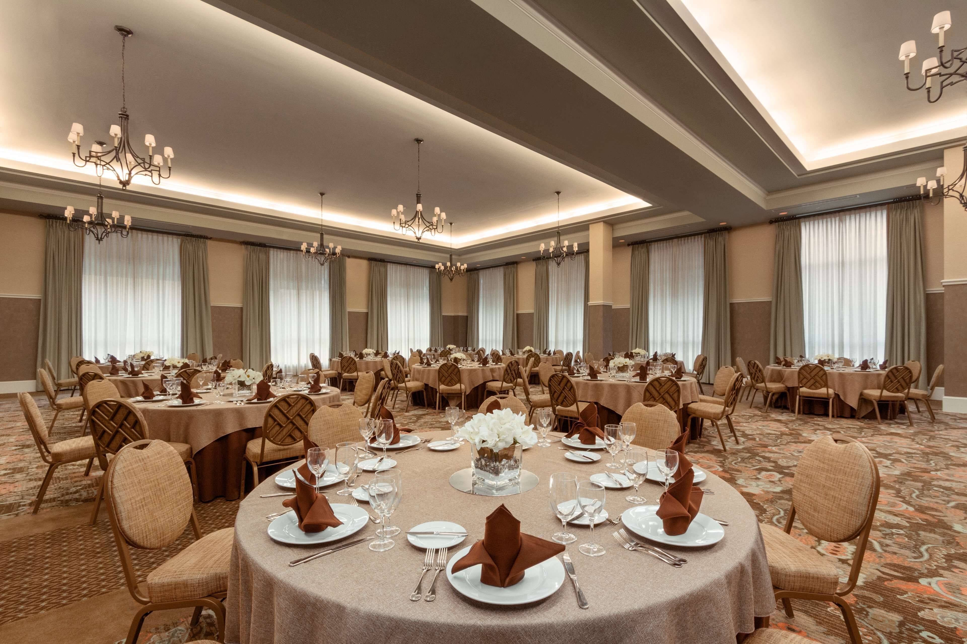 Une salle de banquet avec des tables rondes dressées pour le repas, des lustres et un sol recouvert de moquette.