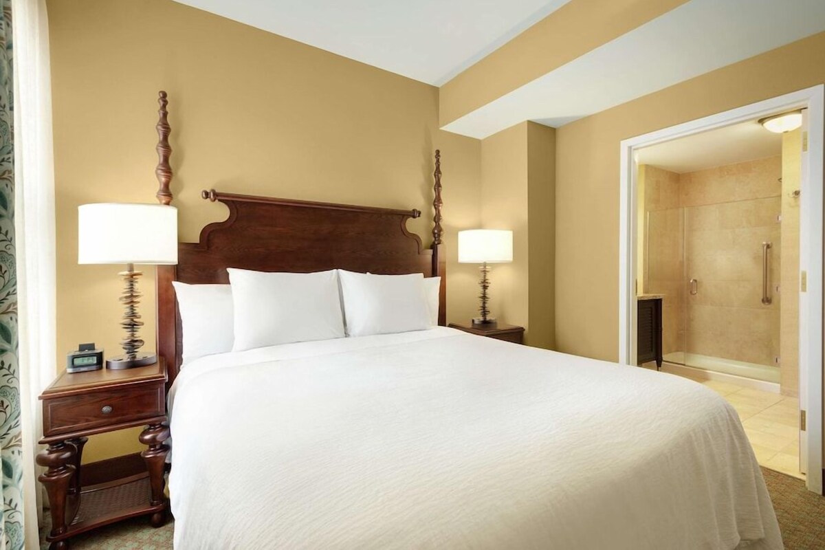 A large bed with a wooden headboard, two bedside tables with lamps, and a door leading to a bathroom.