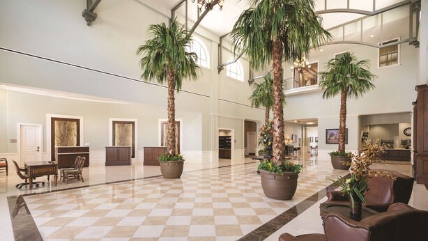 A spacious lobby with a checkered floor, large potted plants, leather seating, and a high ceiling with natural light. - Embassy Suites by Hilton Savannah Historic District (Savannah)