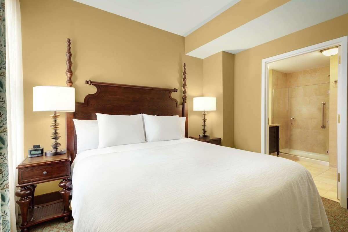 A large bed with a wooden headboard, two bedside tables with lamps, and a bathroom visible through an open door.