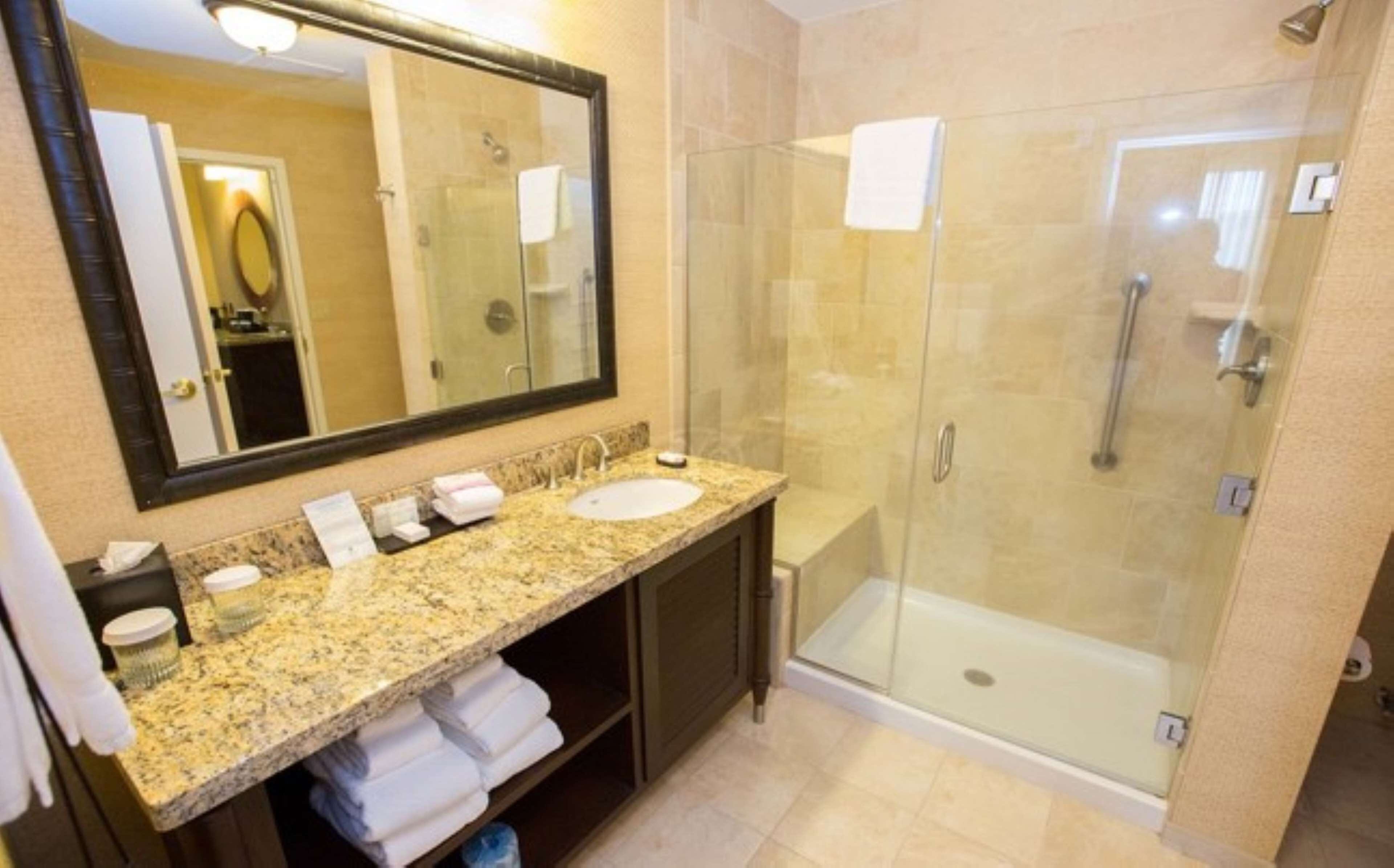 A bathroom with a granite countertop sink, a large mirror, and a glass-enclosed shower.