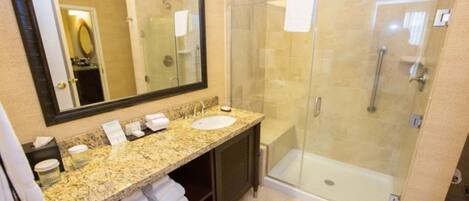 A bathroom with a granite countertop sink, a large mirror, and a glass-enclosed shower.