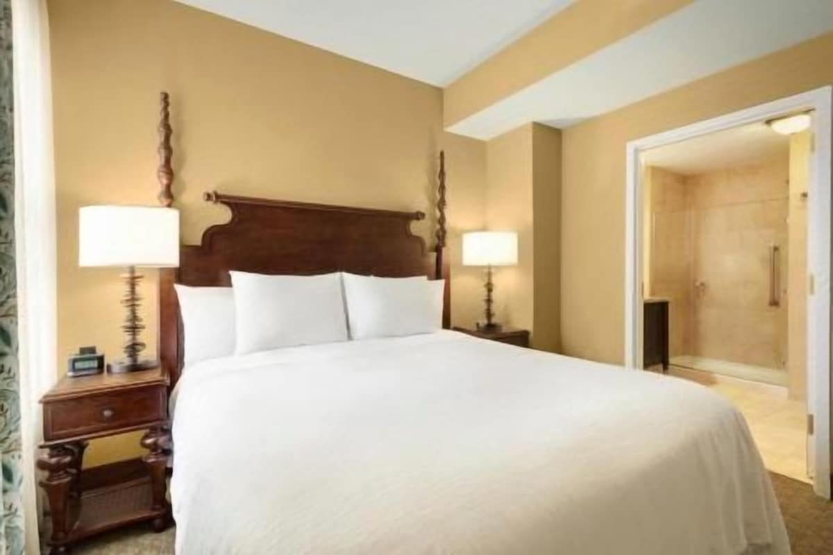 Una habitación de hotel con una cama grande, dos mesitas de noche con lámparas y una puerta que da a un baño.