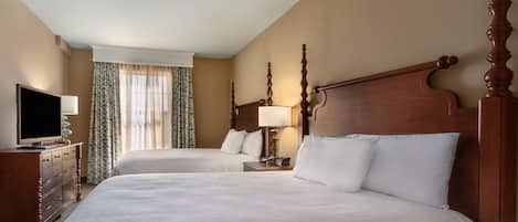 A hotel room with two beds, a TV, a dresser, and a window with curtains.