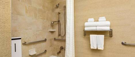 A bathroom with a bathtub, shower, and handrails. There are towels and toiletries on a shelf.