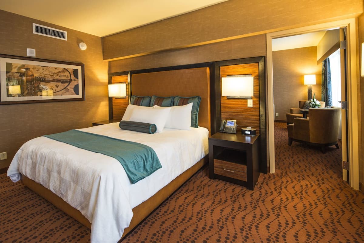 A hotel room with a large bed, a bedside table with a phone, a chair, and a lamp.