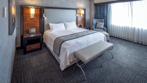 Una habitación de hotel con una cama grande, mesitas de noche con lámparas, una silla y un banco.