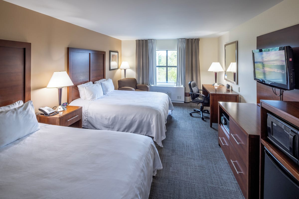 A hotel room with two beds, a desk with a TV, a chair, and a desk lamp.