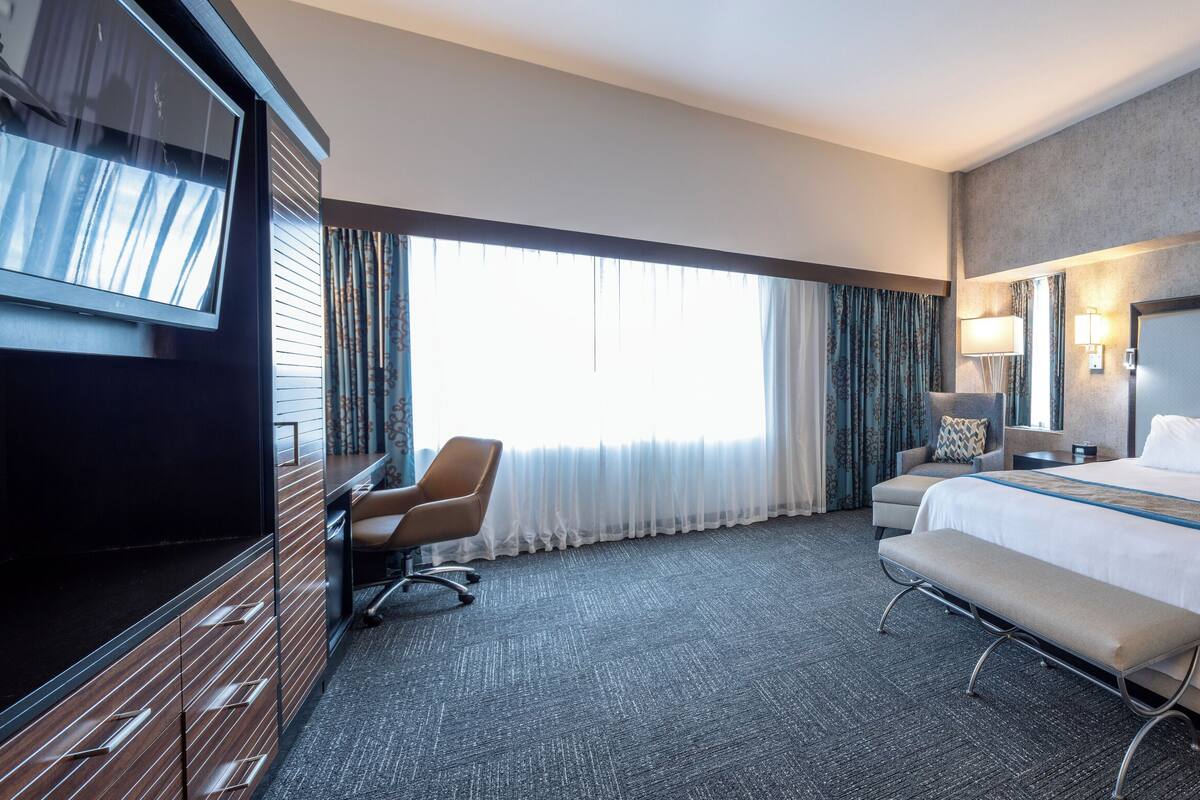 A hotel room with a large bed, a desk, a chair, and a TV.